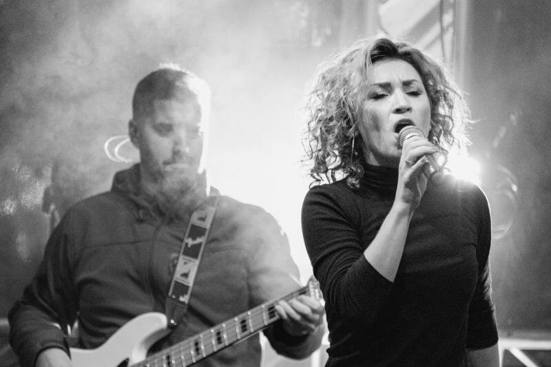 person singing into a microphone while someone plays guitar behind them