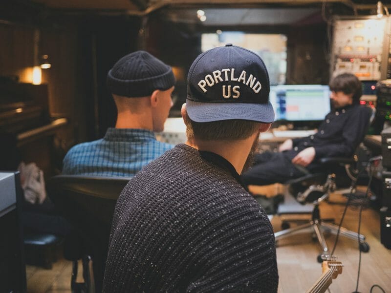 two musicians watching an audio engineer work in a tracking studio